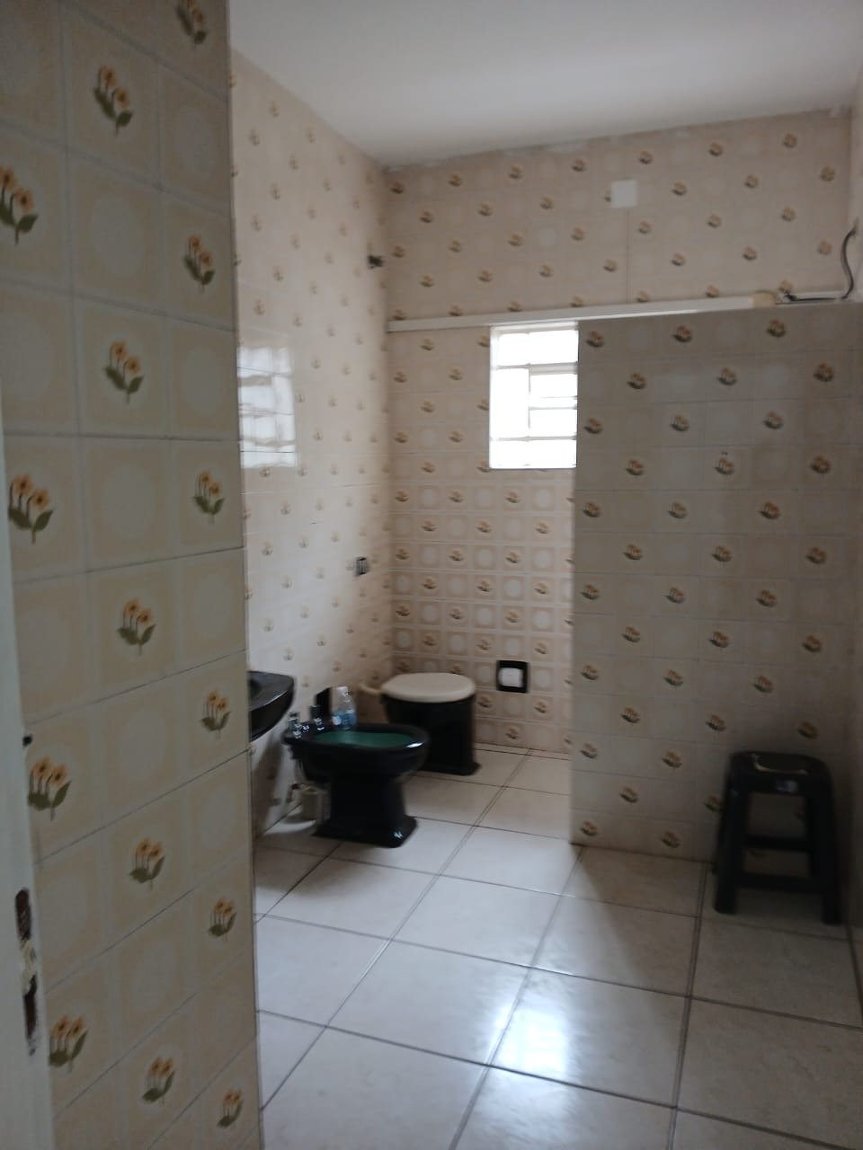 Banheiro do imóvel com azulejo decorado antigo, louças escuras e janela alta.