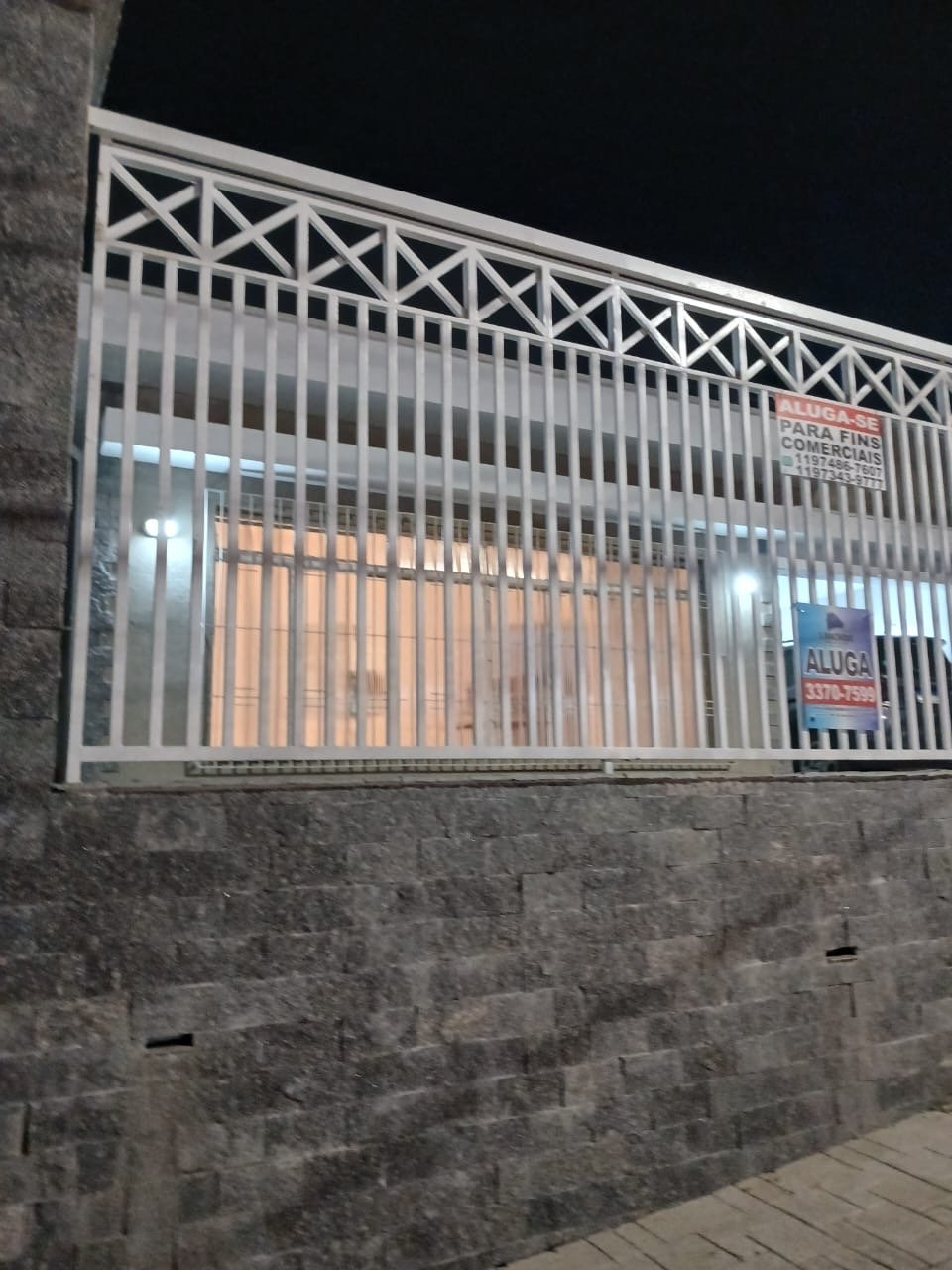 Fachada da casa comercial vista da Avenida Itamarati, com gradeamento branco, muro de pedra e placa de aluga-se para fins comerciais.