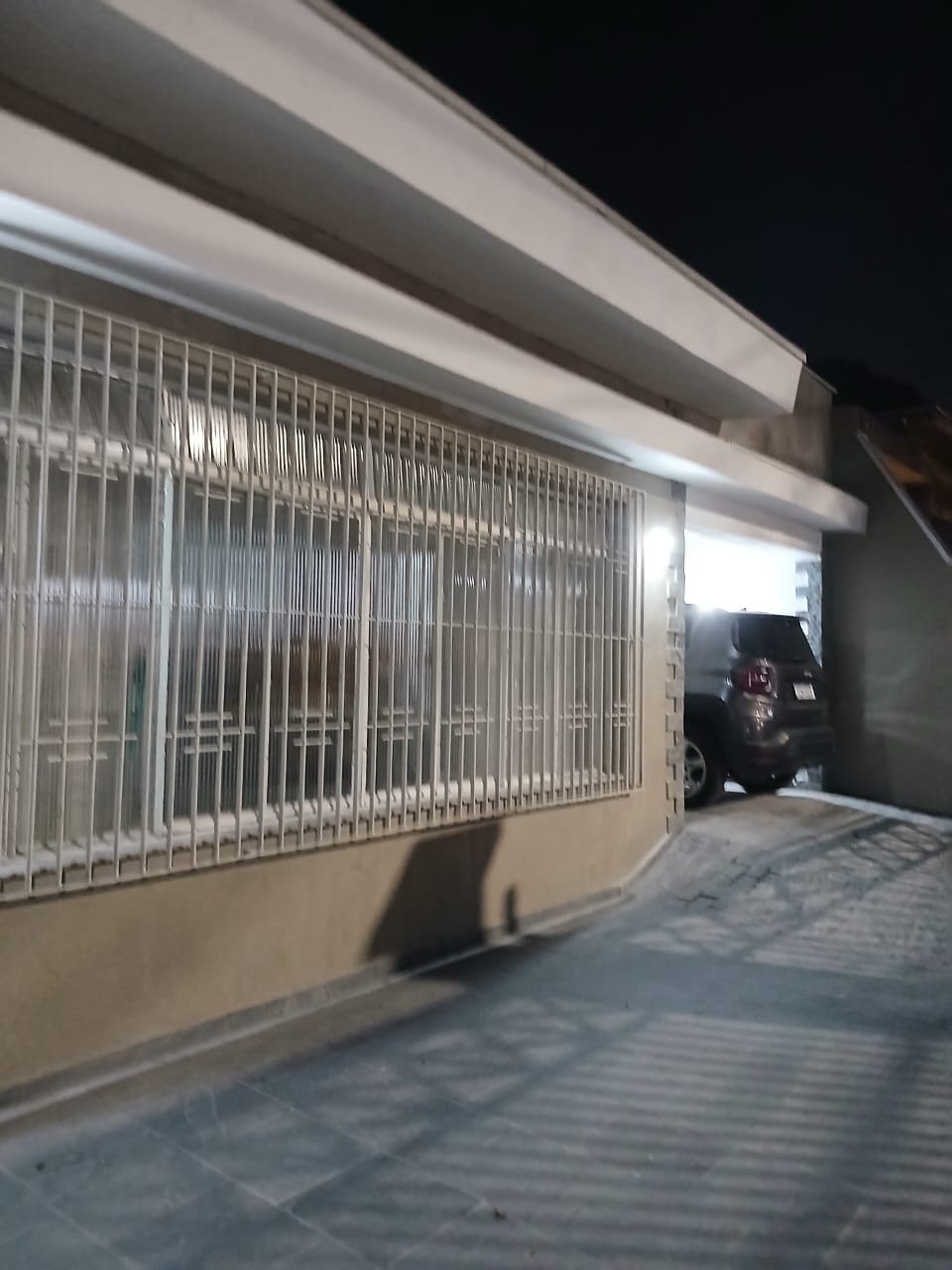 Garagem coberta lateral do imóvel com carro estacionado e acesso para os fundos.