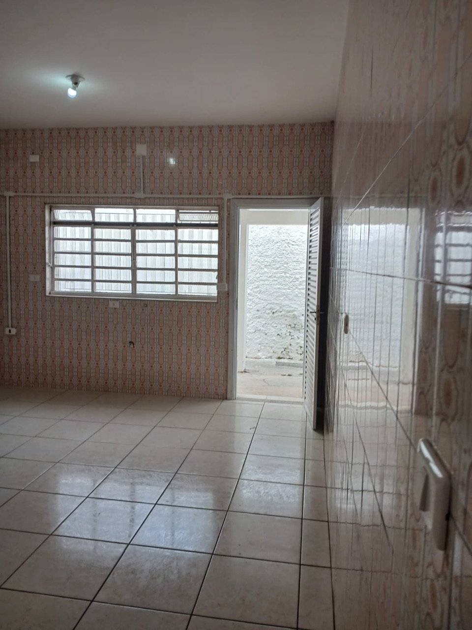 Ambiente dos fundos do imóvel com porta veneziana aberta dando acesso ao quintal descoberto.